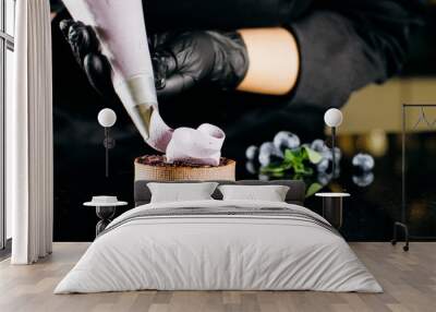 Pastry chef decorates biscuit with purple cream from pastry bag, close-up. Preparation of blueberry cake at commercial bakery with piping bag Wall mural