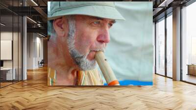 Portrait of senior man playing bamboo flute on the beach next to fishing boat Wall mural