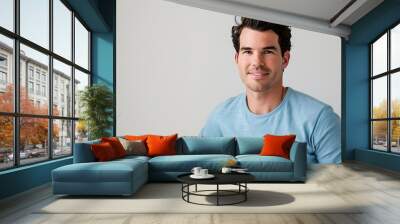 A young man in a blue tshirt smiling in front of a white wall Wall mural