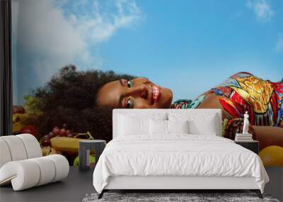 Black woman smiles at the camera while lying among fruits Wall mural