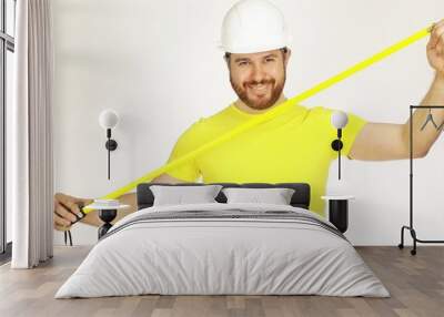 Happy construction engineer or architect in yellow tshirt and hard hat using measure tape against white background Wall mural