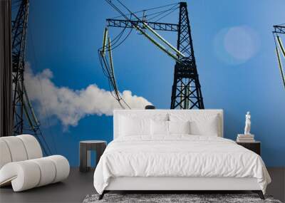 Electric pole with insulators on blue sky and smocking plant chimney background. Wall mural