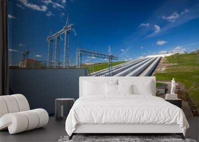 Hydro power plant pipes and electric towers and transformer (left) on blue sky background Wall mural