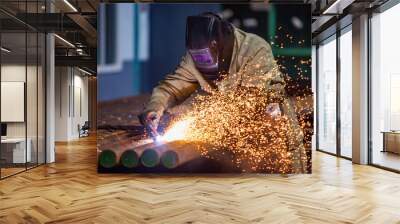 Welder in work in factory. Welding steel pipes on manufacturing (producing) plant. Sparks and smoke on dark background. Wall mural