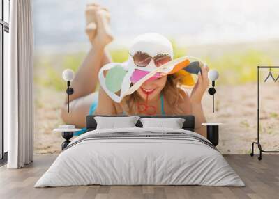 The girl lies on the beach with a glass of juice. Pretty woman 30-35 years old in a blue bikini sunbathes on beach holds juice in her hand. Wall mural