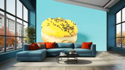 Donut in yellow glaze on blue background/Donut in yellow glaze decorated with dark chocolate decor on blue background. Copy space Wall mural