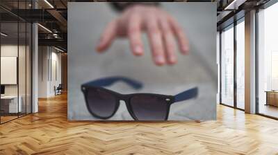 male hand reaching modern sunglasses with blue earpiece Wall mural