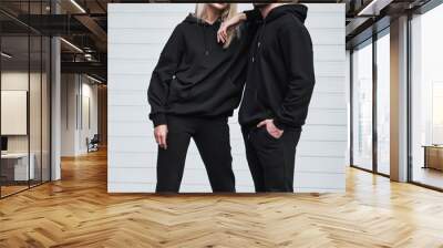 Man and woman wear black hoodies.  A fashion template for print and branding on hoodie. trendy couple on the street wearing casual apparel with no face visible. No logo sweater and pullover with hood. Wall mural