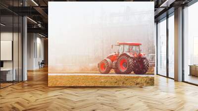 Modern farming tractor working in misty countryside field Wall mural