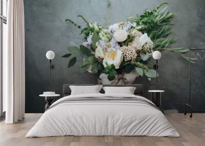 Bridal bouquet. The bride's bouquet. Beautiful bouquet of white, blue, pink flowers and greenery, decorated with long silk ribbon lies on a gray textural background Wall mural