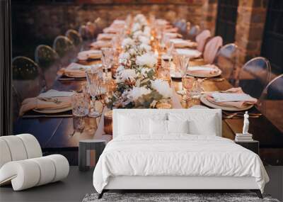 in backyard of villa in Tuscany there is banquet wooden table decorated with cotton and eucalyptus compositions, glasses, burning candles and plates are placed on table, evening Wall mural