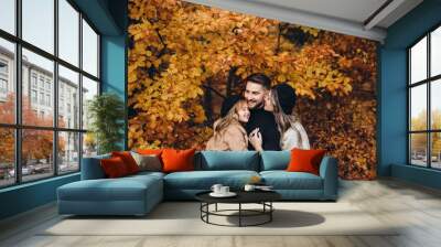 Stylish family in the autumn forest. Models. A young guy and a girl stand on a forest road among yellow leaves and hold their daughter in their arms. Wall mural