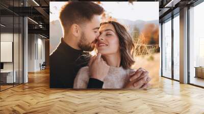 Stylish young couple in the autumn mountains. A guy and a girl hug together under a large old tree on a background of a forest and mountain peaks at sunset. Wall mural