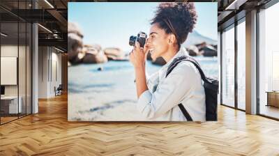 Photographer, woman and camera at beach for travel vacation or holiday in summer sun. Tourist, happy photography and black woman shooting pictures on sea sand for outdoor lifestyle in sunshine Wall mural