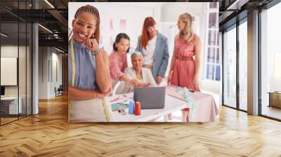 Portrait, designer and fashion with a black woman seamstress standing in her workshop with a team. Fabric, creative and tailor with a female design creative in a studio with a tape measure Wall mural