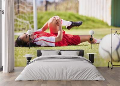 Injured, pain or injury of a female soccer player lying on a field holding her knee during a match. Hurt woman footballer with a painful leg on the ground in agony having a bad day on the pitch Wall mural