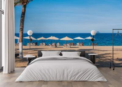 beach umbrellas with sun beds without people on the sandy beach of Nha Trang against the background of the sea or ocean and palm trees. Wall mural