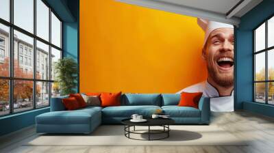 happy male chef in white hat emotionally laughs against an orange isolated background Wall mural