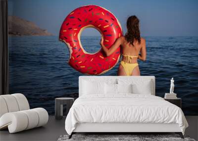 slender woman with a sexy booty in a swimsuit holds an inflatable circle in hands on sunny summer day at sea on vacation Wall mural