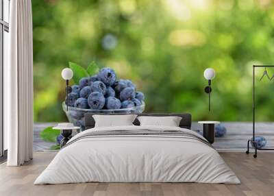 Blueberries in glass bowl and scattered on wooden table Wall mural