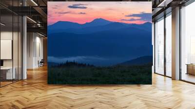 Glowing orange tent in the mountains under dramatic evening sky Wall mural