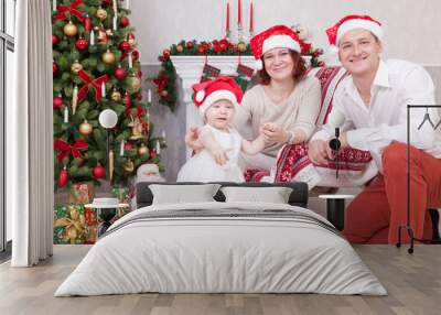 Christmas or New year celebration. Portrait of cheerful young family of three people near the Christmas tree with xmas gifts. A fireplace with christmas stocking on background. Happy holidays Wall mural