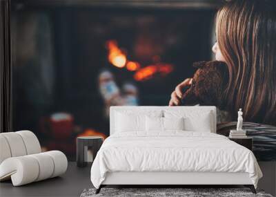 Woman and her Teddy Bear by the fireplace. Unrecognisable relaxes by warm fire with a cup of hot drink and hugging her lovely old handmade toy. Cozy atmosphere. Winter and Christmas holidays concept. Wall mural