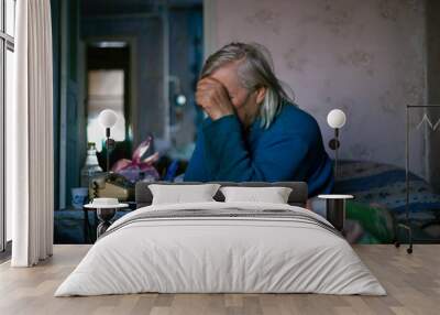 Old poor gray hair woman covered her face with her hand. Woman is sad. Poor life in village. Old age not good. Low-light photo. Wall mural