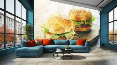 two homemade burgers with green salad leaf, cheese and beef on old rustic wood cutting board in sunlight  Wall mural