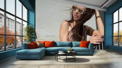 Outdoor portrait of a young beautiful fashionable happy lady, wearing sunglasses, in a wooden frame, creating a city on the street. The model wears stylish clothes. The girl is looking up. Women's Wall mural