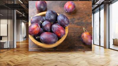 Fresh plums in a wooden bowl on a brown table. Wall mural