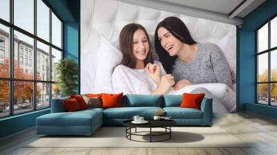 Beautiful mother and her cute teenage daughter laughing, sitting in bed at home Wall mural