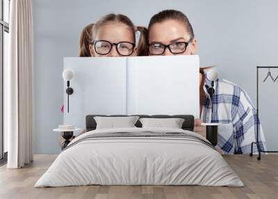 Smiling beautiful woman and her daughter in glasses with book Wall mural