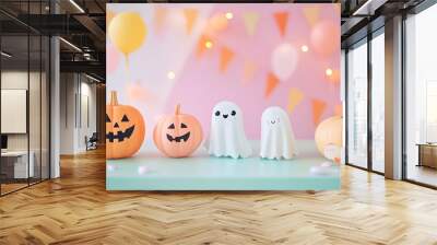 Festive halloween decorations with pumpkins and ghost figures on a table with a soft pink background Wall mural