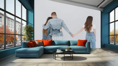 Love triangle. Handsome man embrace his girlfriend while holding hands with another girl. isolated on gray background. Wall mural