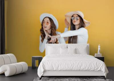 Picture of Two shocked girls pointing and looking away over yellow backgr Wall mural