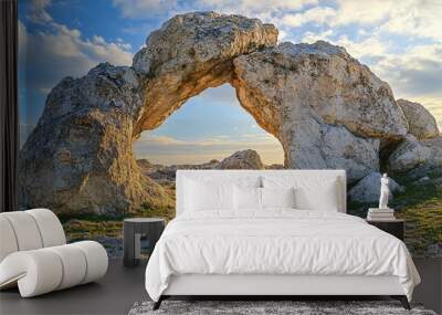 Rocky coastline with a natural rock arch under a sunny sky with white clouds Wall mural