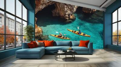 Two individuals paddle kayaks near a rocky ocean cliff with a sunny cave backdrop Wall mural