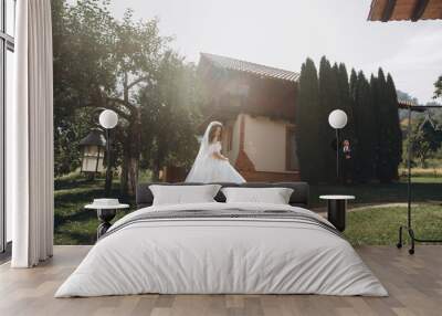 Wedding at an old winery villa in Tuscany, Italy. The bride in a white magnificent dress, with bare shoulders and magnificent sleeves, walks on the garden. Wall mural