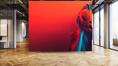 Woman hiding her face behind a scary carved pumpkin on a red background Wall mural