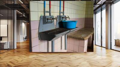 two old metal sinks with hot and cold water taps in the public bath one has a blue basin and a stone bench in the background Wall mural