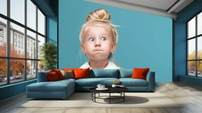 Small, young, funny girl, inflated cheeks on blue background Wall mural