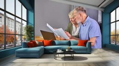 aged couple checking finances at home using laptop, discussing planning budget together, using online banking services and calculator, holding documents in the kitchen Wall mural