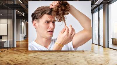 amazed confused man looking at split hair ends, want to cut isolated over light gray background. caucasian young male in casual wear looking embarrassed, need hair care. portrait copy space Wall mural