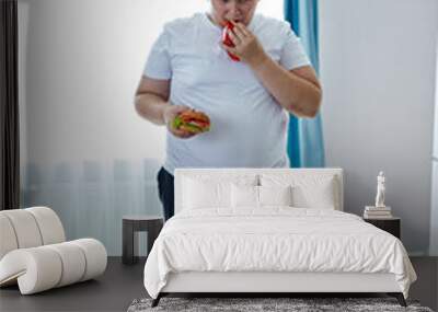 an overweight child suffer from having bad nutrition , stand on scales, look at weight and hold junk food in hands. passive unhealthy lifestyle concept Wall mural