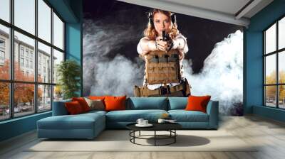 Armed beautiful blonde woman wearing protective headphones and plate carrier, shoots with gun at a target in the darkness with smoke clouds Wall mural