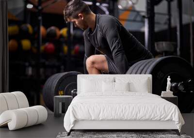 Athlete standing on his knee preparing to make deadlift at gym, young caucasian man in black sportswear engaged in bodybuilding, concentrated on weightlifting. sport, cross fit Wall mural