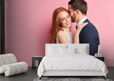 Attractive woman with auburn hair hugging her fiance in elegant suit kissing her. Happy young family, love concept Wall mural