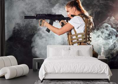 Calm concentrated woman marksman in sniper gear holding rifle in hand aiming at enemy s head in dark smoky background Wall mural