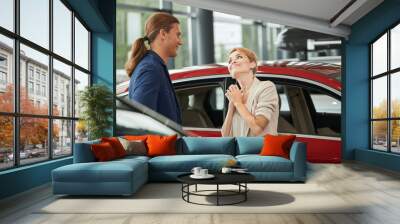 Caucasian blonde woman begging her boyfriend to buy luxury car in the dealership. Wall mural